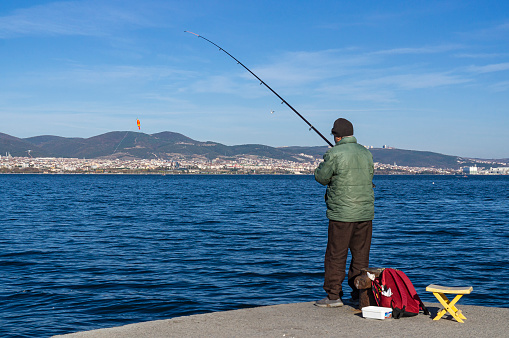 Degirmendere, Kocaeli, Turkey - December 14, 2019: Single fisherman catches fish from the pier with a fishing rod. Turkey, sunny winter day
