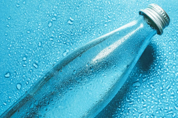 A glass bottle of water on blue background splashes drops of water on top. Quench thirst. Background water drops place for text copy space A glass bottle of water on blue background splashes drops of water top. Quench thirst. Background water drops place for text copy space quench your thirst pictures stock pictures, royalty-free photos & images