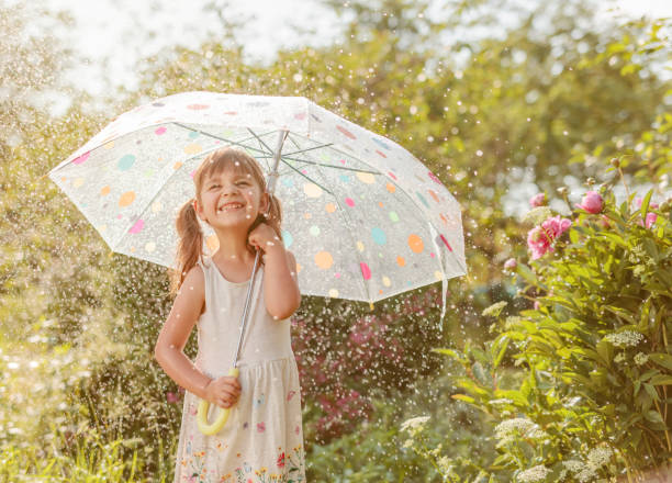 petite fille heureuse dans le jardin sous la pluie d’été avec un parapluie. - under the weather photos et images de collection