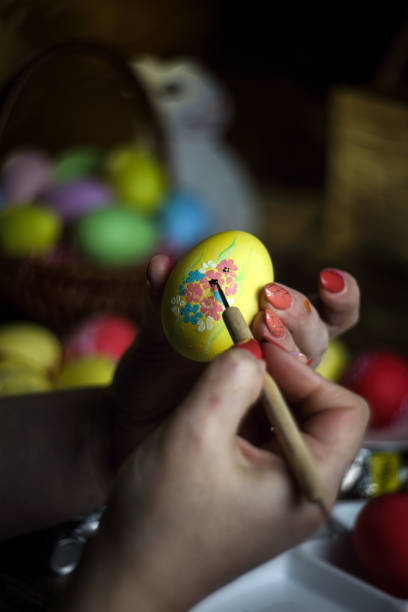 istock Woman hands painting eggs with floral patterns. Preparing for Easter. Artist paints an Easter egg. Close-up. Selective focus. Copy space. Vertical orientation. 1216262493