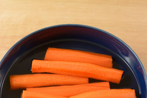 Close up of peeled and cut carrots soaking in water on blue bowl to preserve freshness
