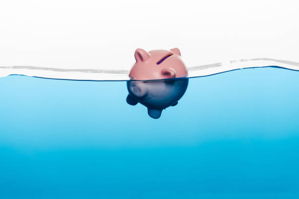 istock piggy bank going under blue water isolated on white, coronavirus crisis concept 1216271075