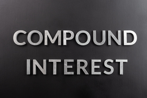 the words compound interest laid with silver metal letters on matte black surface in flat lay composition, directly above view