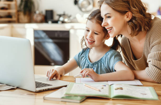 Happy girl with mother studying online at home Positive young woman helping daughter in searching information for homework on internet while sitting together at table with laptop at home one parent stock pictures, royalty-free photos & images