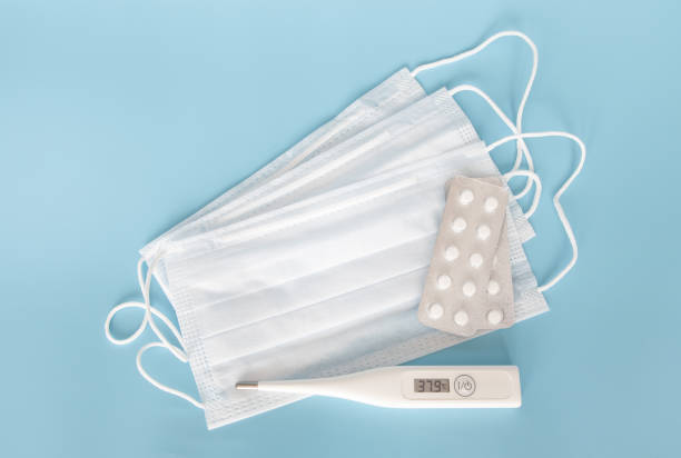 istock Modern thermometer with an electronic dial and a high temperature indicator, next to a medical mask and pills on a blue background. 1216277281