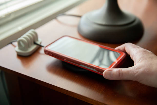 istock Woman's hand holding mobile cell phone on a wireless charger on a nightstand table with a cord keeper for organization of technology 1216278343