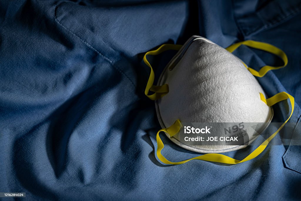 Closeup of N95 Mask on Blue Scrubs N95 PPE protective mask resting on blue medical scrubs with copy space N95 Face Mask Stock Photo