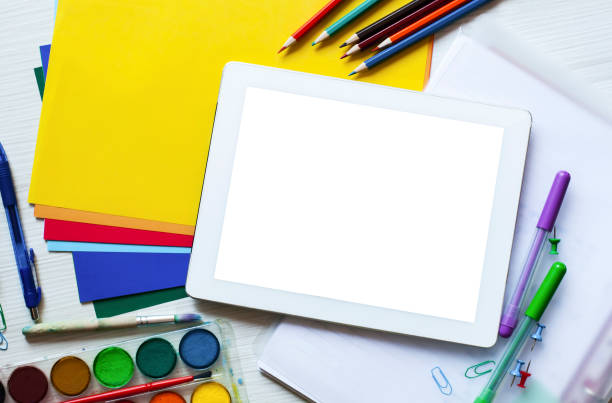 istock School set and office supplies set with digital tablet with blank white desktop screen, pencils, colored paper, paint, scissors, figures and glasses on white wooden background. 1216284518