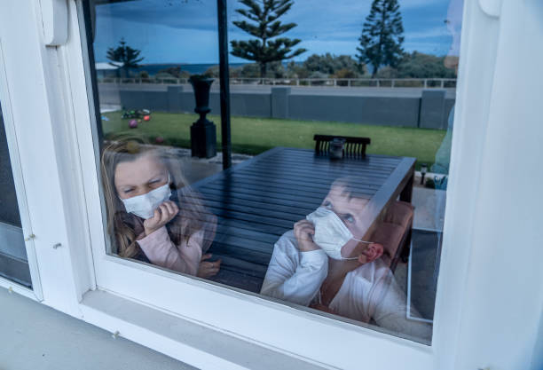 istock COVID-19 Lockdowns. Sad children with face mask looking through the window during quarantine at home. Kids feeling sad as school is closed. Coronavirus outbreak isolation and kids mental health. 1216289523