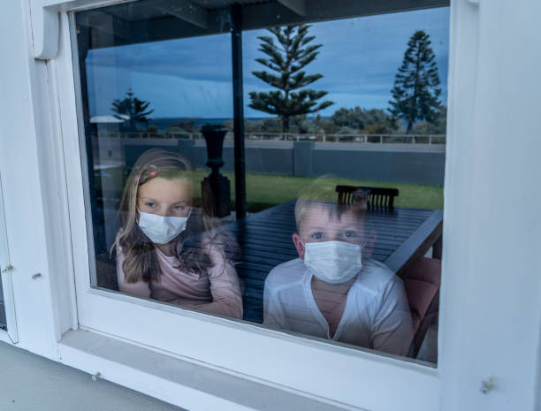 istock COVID-19 Lockdowns. Sad children with face mask looking through the window during quarantine at home. Kids feeling sad as school is closed. Coronavirus outbreak isolation and kids mental health. 1216289552