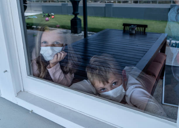 istock COVID-19 Lockdowns. Sad children with face mask looking through the window during quarantine at home. Kids feeling sad as school is closed. Coronavirus outbreak isolation and kids mental health. 1216289620