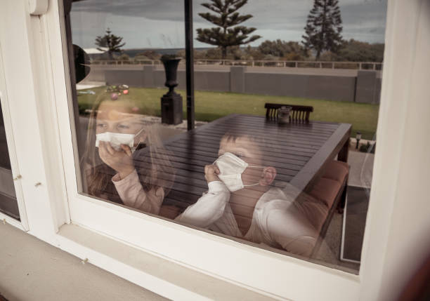 istock COVID-19 Lockdowns. Sad children with face mask looking through the window during quarantine at home. Kids feeling sad as school is closed. Coronavirus outbreak isolation and kids mental health. 1216289621