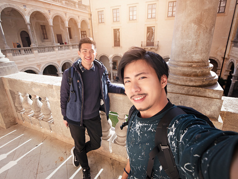 2 Asian tourist backpackers traveling through Italy and taking selfies.