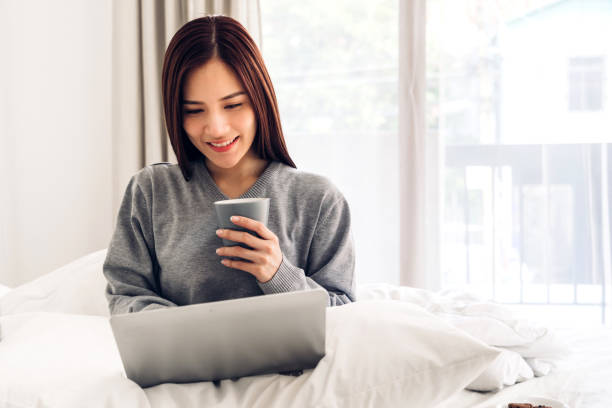 istock Young woman relaxing and drinking cup of hot coffee or tea using laptop computer on a cold winter day in the bedroom.woman checking social apps and working.Communication and technology concept 1216312322
