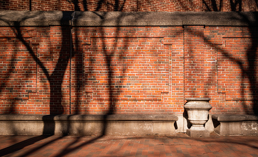 Rustic red brick wall, stone bench and stone flower vase with tree shadows