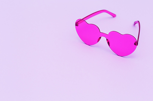 Stylish heart shaped glasses on paper background with copy space. Beautiful trendy purple sunglasses. Fashion summer concept.