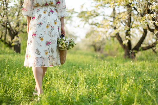 A girl walks through a spring green park enjoying the blooming nature.