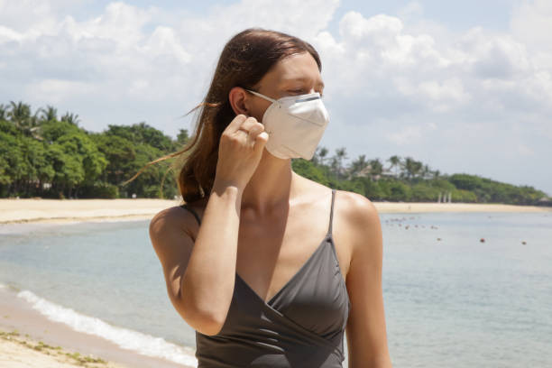 istock Woman with disposable surgical mask alone on the beach. Empty beach during coronavirus lockdown. Coronavirus pandemic crisis. Tourism is entering a great crisis due to the worldwide panic of the Corona Virus. 1216332591