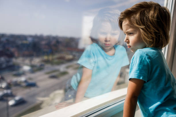 istock Sad little boy looking through window from home. 1216334464