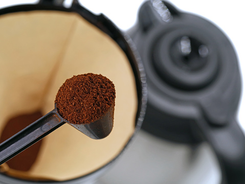 spoon with coffee powder in front of coffee strainer with coffee pot on background. concept of making coffee for breakfast.
