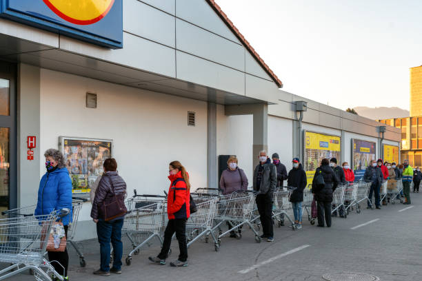 People  with face masks and  shopping carts in front of grocery RUZOMBEROK, SLOVAKIA - APRIL 2: Long line of people  with face masks and  shopping cart in front of grocery editorial stock pictures, royalty-free photos & images