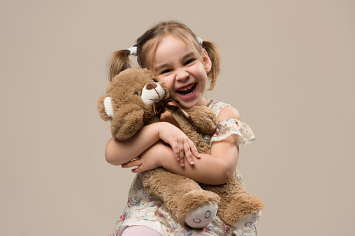 Little girl putting coins in her pink piggy bank in front of white background