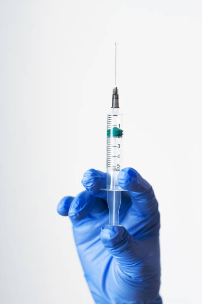 A hand in blue protective gloves holds a syringe containing an antiviral vaccine stock photo