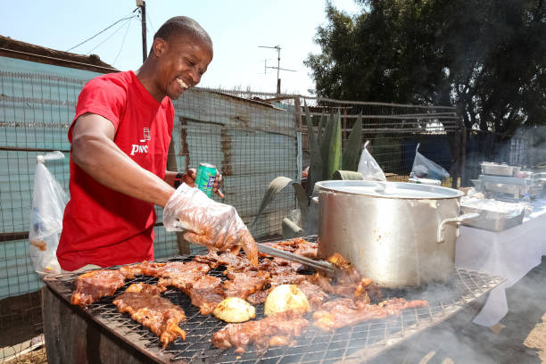 African man working a BBQ Grill on side street in urban Soweto Soweto, South Africa - September 10, 2011: African man working a BBQ Grill on side street in urban Soweto south african braai stock pictures, royalty-free photos & images