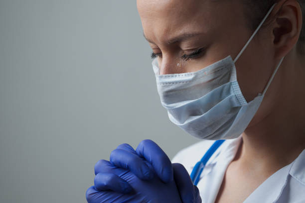 una dottoressa terapista in veste bianca, maschera e guanti. faccia da vicino. il dottore piange e prega. lacrime agli occhi. pandemia ed epidemia di virus. coronavirus covid-19. - doctor emotional stress worried healthcare and medicine foto e immagini stock