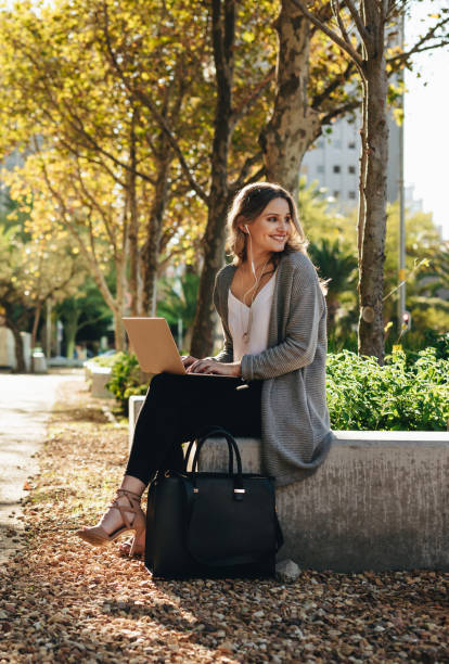 istock Smiling woman sitting outdoors with laptop 1216346549