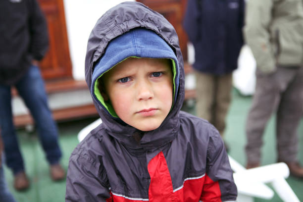 June 29, 2013 - Norway: Headshot of a serious worried handsome boy in rain jacket with hoodie on standing on a boat, looking at camera being cold and lonely