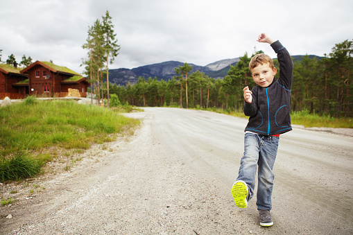 June 28, 2013 - Norway:Funny cute little boy, toddler, walking alone on a dirt road in Norway, lifting his foot to show the sole of his shoe.