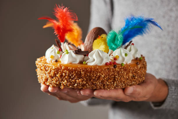 mona de pascua, Easter cake eaten in Spain closeup of a caucasian man with a typical mona de pascua, a cake eaten in Spain on Easter Monday, decorated with a chocolate egg, a plush chick and feathers of different colors, in his hands godfather godparent stock pictures, royalty-free photos & images