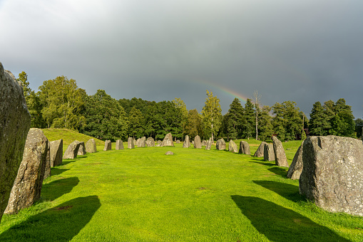Formation of megaliths at an old burial ground in Anundshög in Sweden. In summer sunlight and a gray overcast sky with a rainbow.