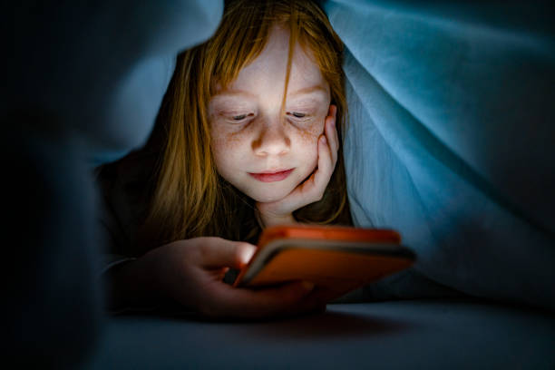 chica usando el teléfono móvil en la cama en la oscuridad - one kid only fotografías e imágenes de stock