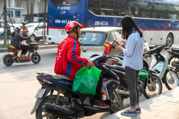 Now bike delivery man giving drinks and foods Hanoi, Vietnam - Mar 21, 2019: Now bike delivery man giving drinks and foods to recipient at Dao Tan street vietnamese man taxi motorbike driver stock pictures, royalty-free photos & images