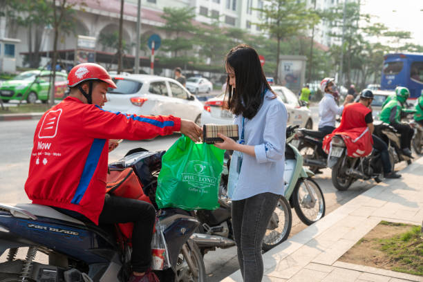 Now bike delivery man giving drinks and foods Hanoi, Vietnam - Mar 21, 2019: Now bike delivery man giving drinks and foods to recipient at Dao Tan street vietnamese man taxi motorbike driver stock pictures, royalty-free photos & images