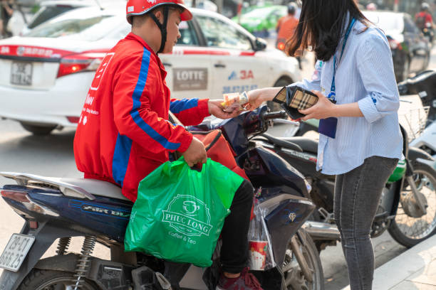 Now bike delivery man giving drinks and foods Hanoi, Vietnam - Mar 21, 2019: Now bike delivery man giving drinks and foods to recipient at Dao Tan street vietnamese man taxi motorbike driver stock pictures, royalty-free photos & images