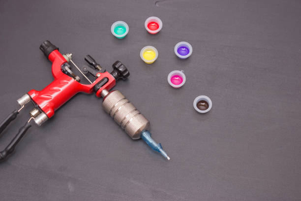istock Rotary tattoo machine and disposable plastic jars with colored paints on a black background. Free space for text. Top view. Banner 1216356118