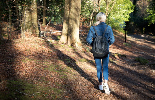 istock A typical Millennial Generation blond young woman, walking through the forest for a stroll. She is wearing a denim jacket and scarring a backpack. She is modern and fashionable. 1216363464