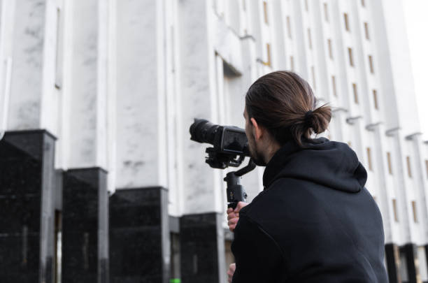 istock Young Professional videographer holding professional camera on 3-axis gimbal stabilizer. Pro equipment helps to make high quality video without shaking. Cameraman wearing black hoodie making a videos. 1216365157