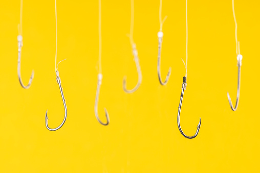 Fishing hooks are hanging with transparent string in front of yellow background.