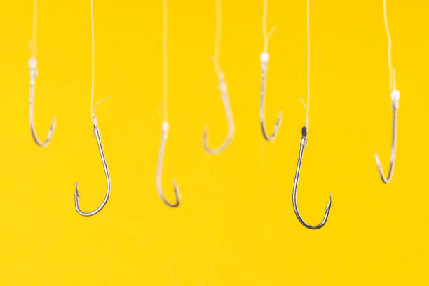 Fishing Hooks Fishing hooks are hanging with transparent string in front of yellow background. temptation photos stock pictures, royalty-free photos & images