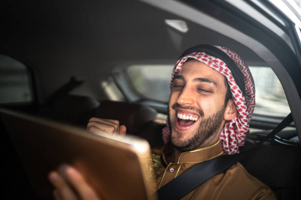 arabische mens van het midden-oosten die sporten let met behulp van digitale tablet binnen een auto - qatar football stockfoto's en -beelden
