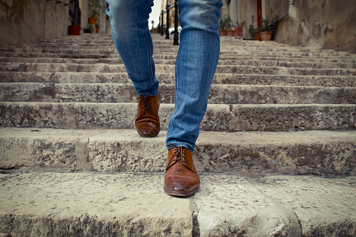 One men in brown shoes walking down outdoor stairway in city, detail of his legs