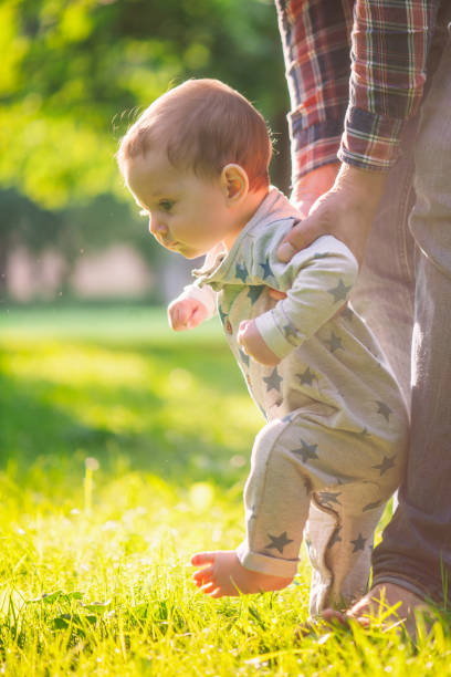 Father helping his baby boy to make first steps on green grass