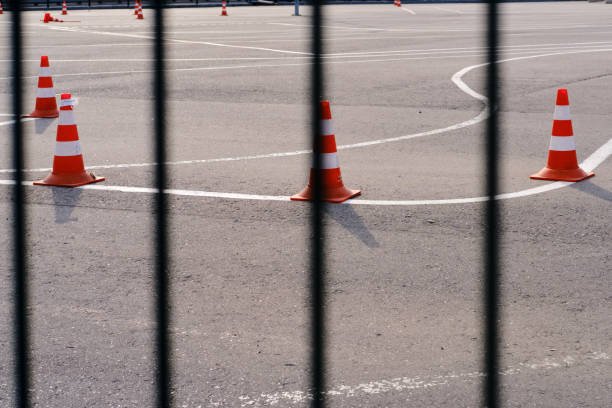 istock Fence with bars and a school for training drivers, lines with cones on the pavement. Closed because of the coronavirus epidemic, a driving training ground. 1216379384