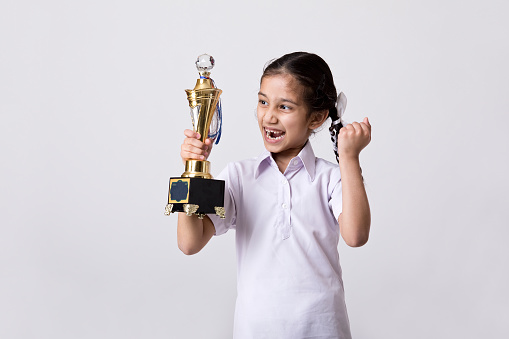 Cheerful schoolgirl holding trophy and celebrating victory over white background