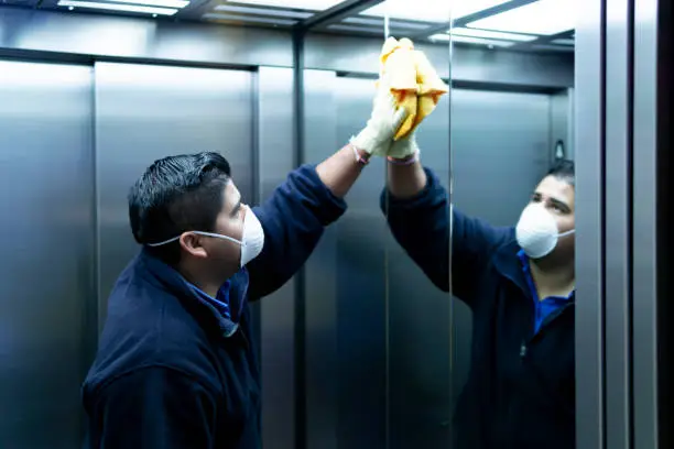 Photo of coronavirus. cleaning staff disinfecting elevator to avoid contagion
