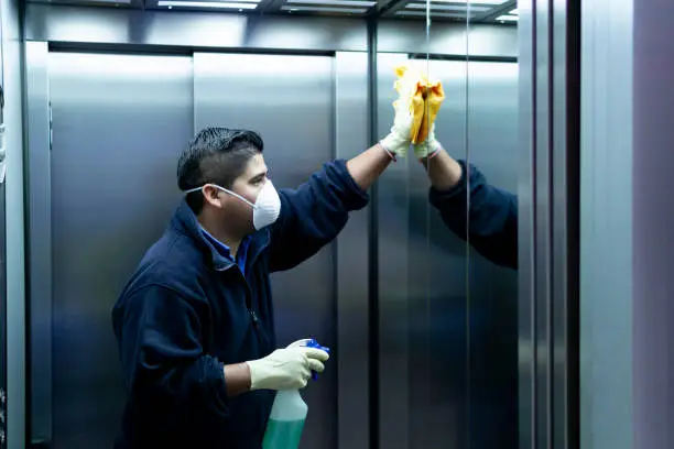 Photo of coronavirus. cleaning staff disinfecting elevator to avoid contagion